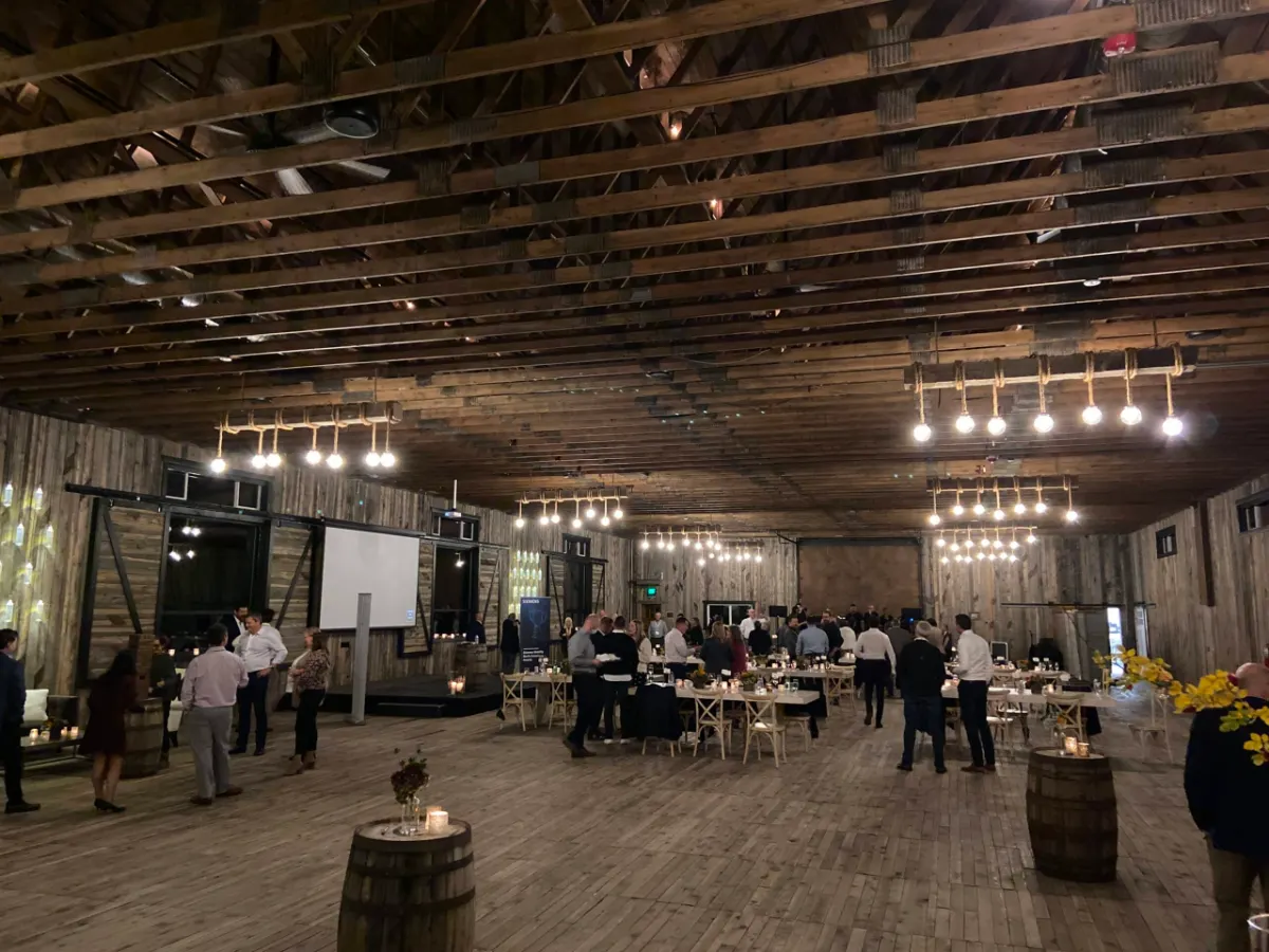 Guests seated at round tables under warm string lighting in the barn