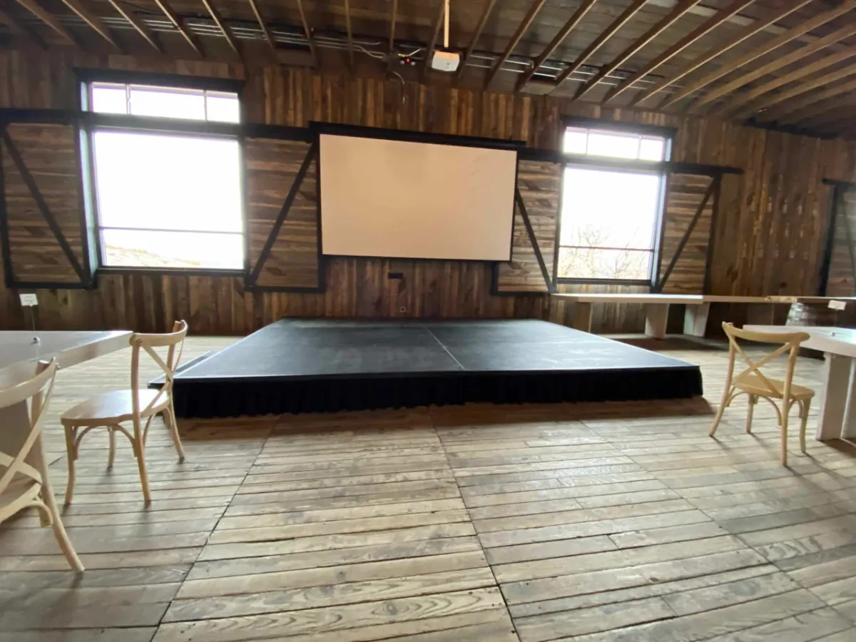 Black stage deck set below a projection screen in the timber barn at Blue Sky Lodge