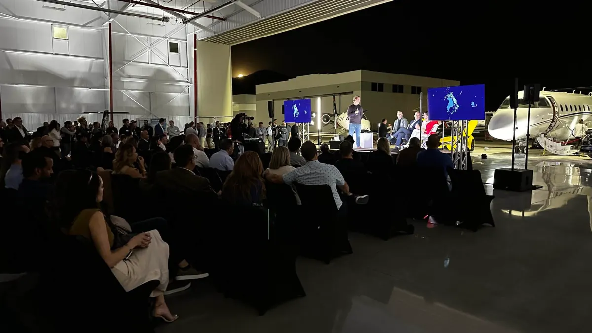 Guests seated in front of the stage and screens under blue lighting inside the Provo Airport hangar