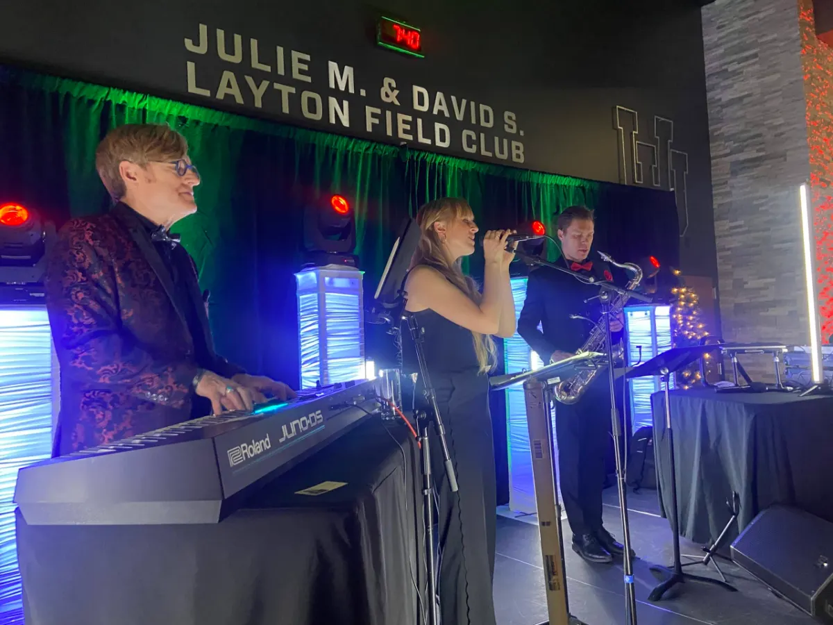 DJ, keyboard player, saxophonist and vocalist performing together under blue stage lighting at the Ken Garff Red Zone