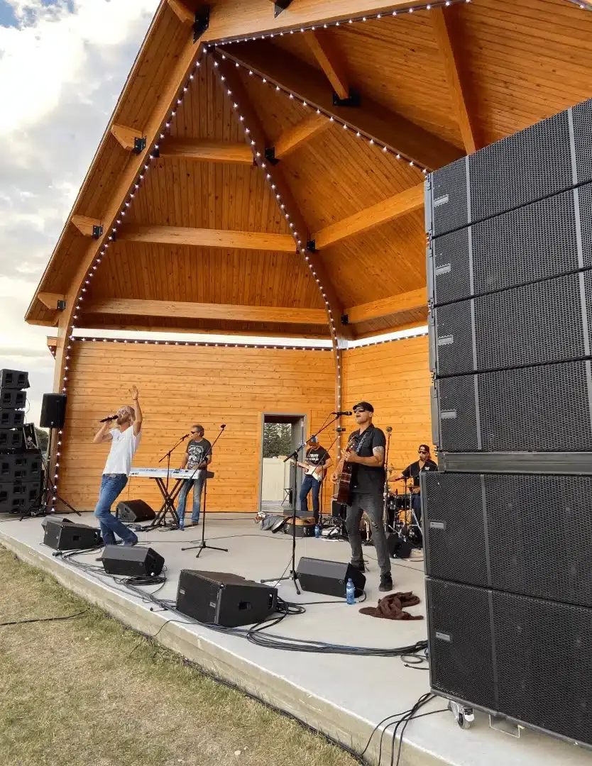 Outdoor pavilion stage with line array speakers flying either side of the band