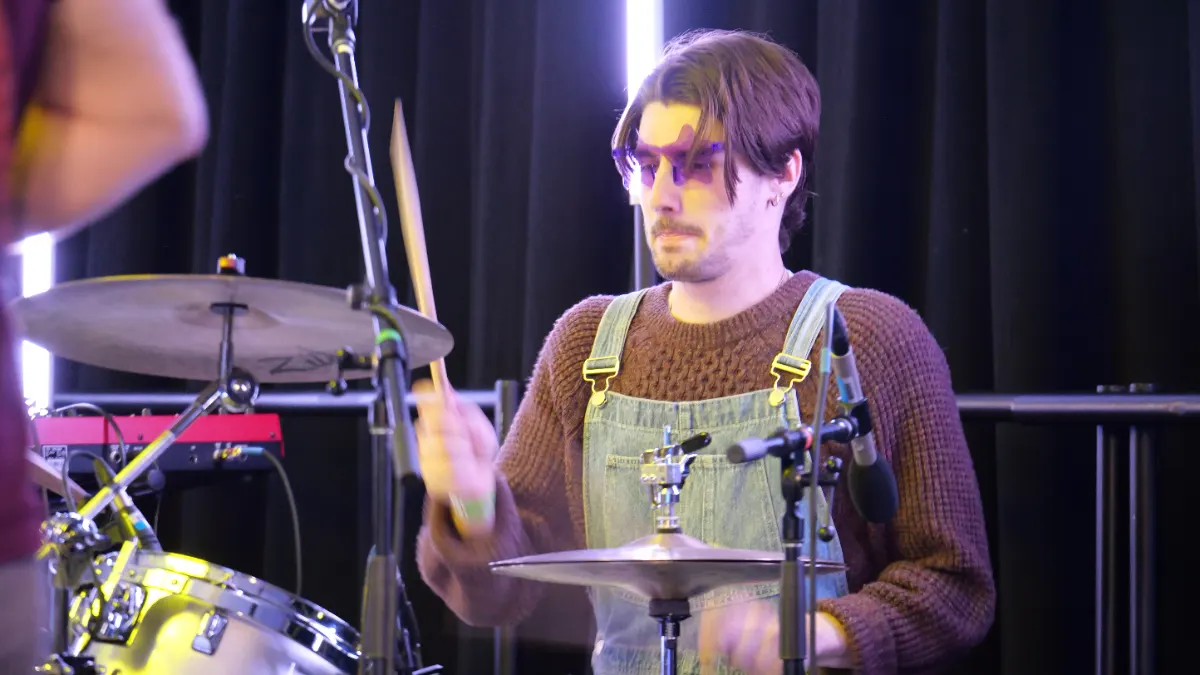 Drummer mid-set behind a miked kit under stage lighting