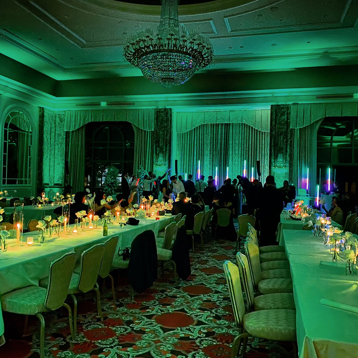 Grand America ballroom washed in green uplighting with long banquet tables and a chandelier