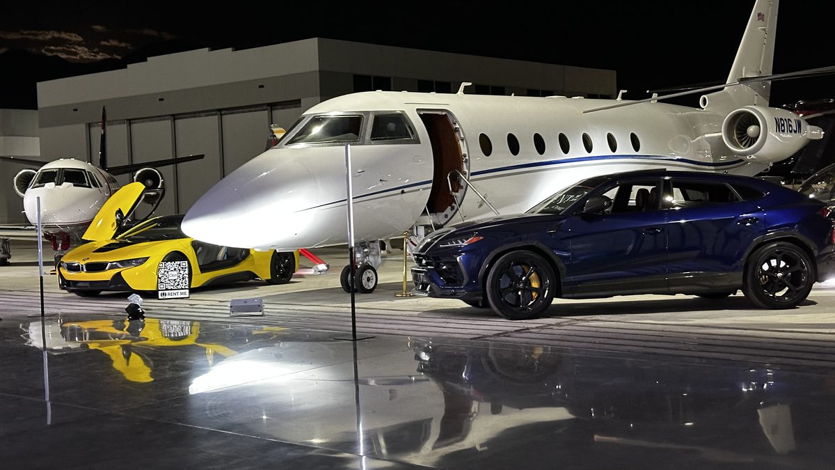 A private jet and sports cars dramatically uplit at a hangar event at night