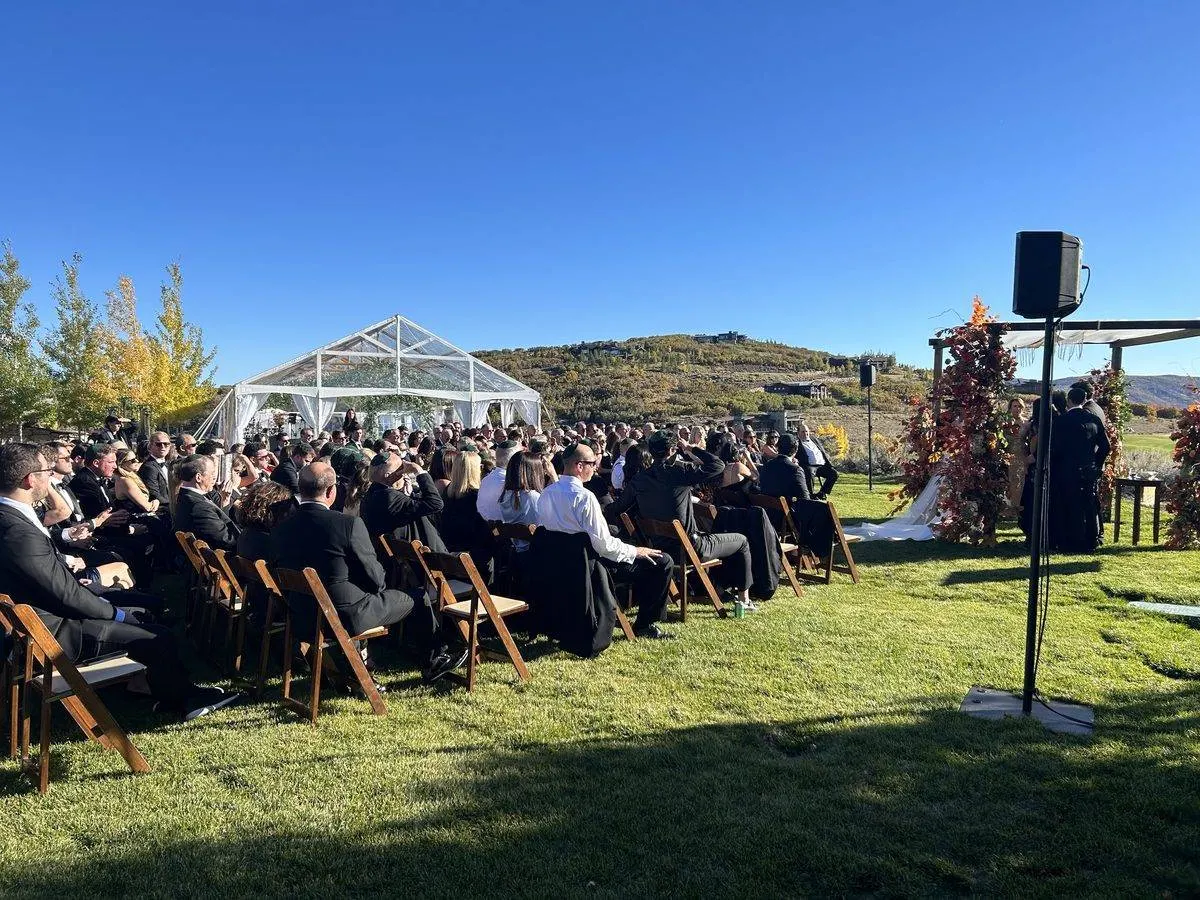 Outdoor ceremony sound with a discreet speaker on a stand under a clear-top tent and mountain backdrop