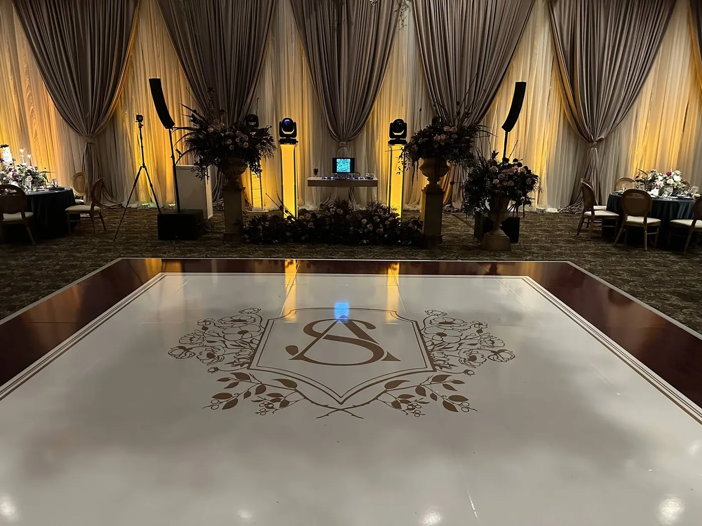 Draped ballroom with monogrammed white dance floor and warm uplighting